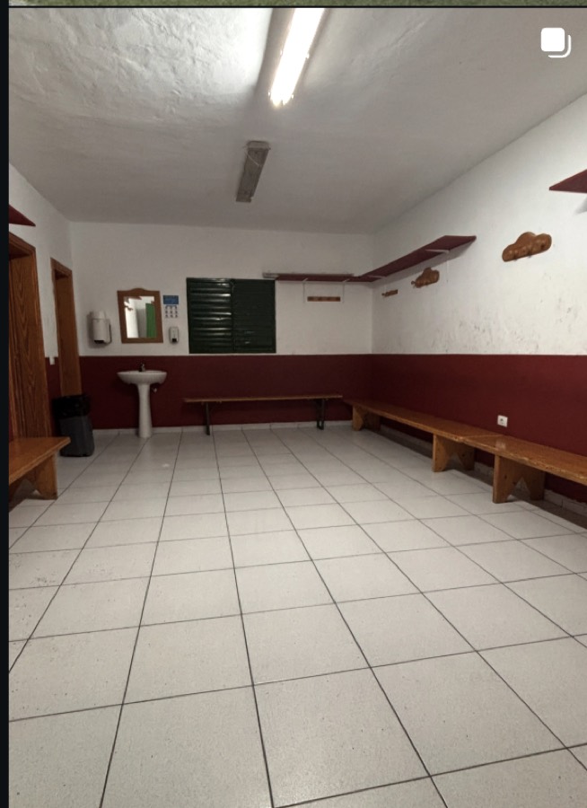 Vestuario del club: alicatado blanco, bancos de madera y perchas en la pared